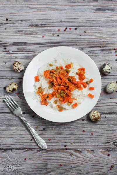 Вкусный рис с тушеной морковью, горох и лук на белой тарелке, перепелиные яйца, перец и вилка на светлом деревянном столе — стоковое фото