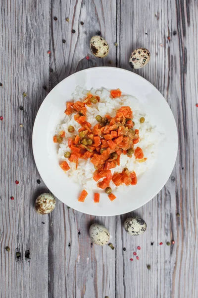 haşlanmış havuç, bezelye ve soğanlı bir beyaz tabak, bıldırcın yumurtası, biber ve ahşap masa lambası çatalı ile lezzetli pirinç