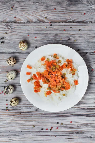 Вкусный рис с тушеной морковью, горох и лук на белой тарелке, перепелиные яйца, перец и вилка на светлом деревянном столе — стоковое фото