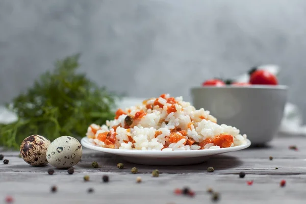 Вкусный рис с тушеной морковью, горох и лук на белой тарелке, перепелиные яйца, миска с помидорами черри, полотенце, перец и укроп на светлом деревянном столе — стоковое фото