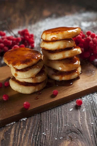 syrups with powdered sugar on a wooden cutting board, a sieve of a viburnum berry and caramel topping on a dark wooden table