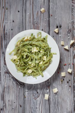 Spagetti ıspanak yeşil Mozzarella peyniri ile hafif ahşap masa üzerinde beyaz bir plaka üzerinde otlar ile