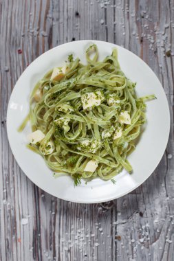 Spagetti ıspanak yeşil Mozzarella peyniri ile hafif ahşap masa üzerinde beyaz bir plaka üzerinde otlar ile