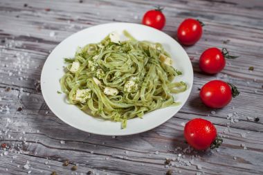 Mozzarella peyniri, otlar ve ahşap masa lambası üzerinde beyaz bir tabakta domates yeşil ıspanaklı makarna