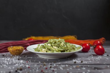 Mozzarella peyniri, otlar ve ahşap masa lambası üzerinde beyaz bir tabakta domates yeşil ıspanaklı makarna