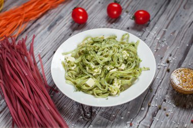 Mozzarella peyniri, otlar ve ahşap masa lambası üzerinde beyaz bir tabakta domates yeşil ıspanaklı makarna