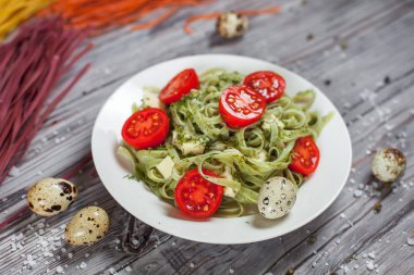 Mozzarella peyniri, yeşillik ve Fransız hardalı, bıldırcın yumurtası ve kiraz domates bir plaka, biber ve karanlık bir arka plan üzerinde gri bir ahşap masa üzerinde büyük deniz tuzu ile yeşil ıspanaklı makarna