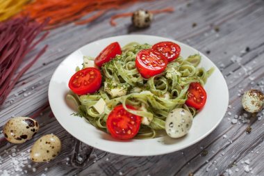 Mozzarella peyniri, yeşillik ve Fransız hardalı, bıldırcın yumurtası ve kiraz domates bir plaka, biber ve karanlık bir arka plan üzerinde gri bir ahşap masa üzerinde büyük deniz tuzu ile yeşil ıspanaklı makarna