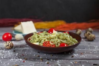 Mozzarella peyniri, yeşillik ve Fransız hardalı, bıldırcın yumurtası ve kiraz domates bir plaka, biber ve karanlık bir arka plan üzerinde gri bir ahşap masa üzerinde büyük deniz tuzu ile yeşil ıspanaklı makarna