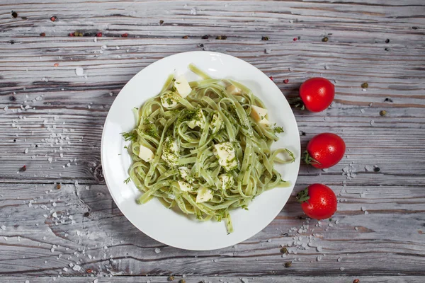 Spaghetti agli spinaci verdi con mozzarella, erbe aromatiche e pomodoro su un piatto bianco su un tavolo di legno chiaro — Foto Stock