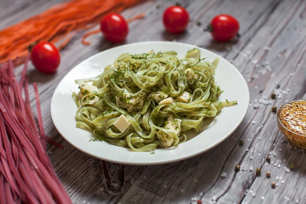 Espaguete com espinafre verde com mussarela, ervas e tomate em uma placa branca em uma mesa de madeira leve — Fotografia de Stock