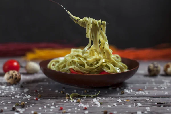 Pasta from green spinach with mozzarella, greens and French mustard, quail eggs and cherry tomatoes on a plate, bell pepper and large sea salt on a gray wooden table on a dark background — Stock Photo, Image