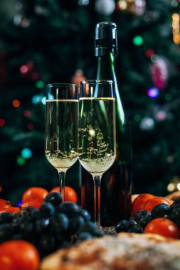 bir yeni yıl'ın tablo, peynir pasta çikolata, mandalina, üzüm, bisküvi, şampanya ve iki bardak dekore edilmiş bir Noel ağacı ışıkları ile fon karşı