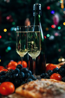 bir yeni yıl'ın tablo, peynir pasta çikolata, mandalina, üzüm, bisküvi, şampanya ve iki bardak dekore edilmiş bir Noel ağacı ışıkları ile fon karşı