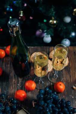 bir yeni yıl'ın tablo, peynir pasta çikolata, mandalina, üzüm, bisküvi, şampanya ve iki bardak dekore edilmiş bir Noel ağacı ışıkları ile fon karşı