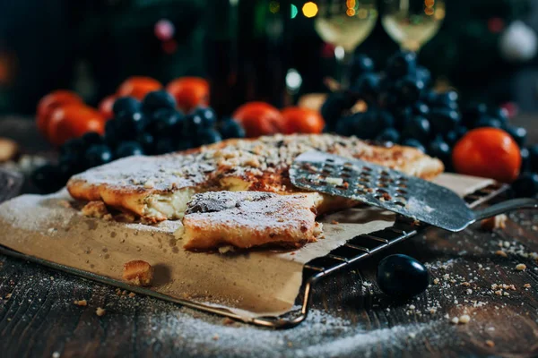 Una mesa de Año Nuevo festiva, pastel de queso con chocolate, mandarinas, uvas, galletas, champán y dos copas en el contexto de un árbol de Navidad decorado con luces — Foto de Stock