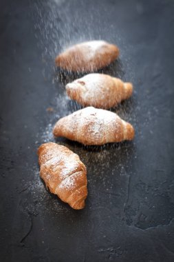 bir meyve dolgulu dört ay çöreği ile koyu gri arka plan üzerine pudra şekeri serpilir