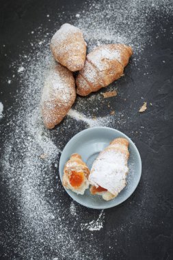 bir meyve dolgulu dört ay çöreği ile koyu gri arka plan üzerine pudra şekeri serpilir