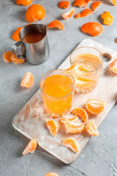 orange drink, tangerines, white cutting board on light gray background