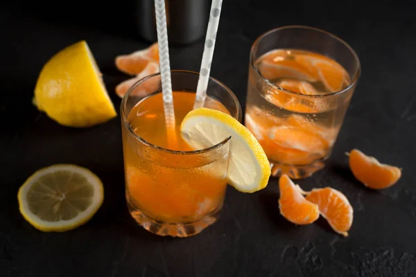 Bebida cor-de-laranja, tangerinas e limão sobre um fundo escuro — Fotografia de Stock