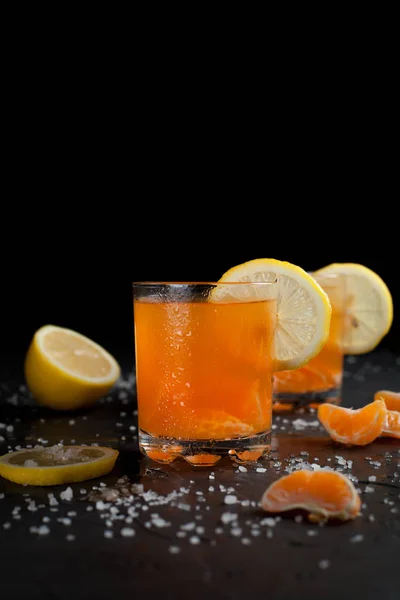 Bebida cor-de-laranja, tangerinas e limão sobre um fundo escuro — Fotografia de Stock