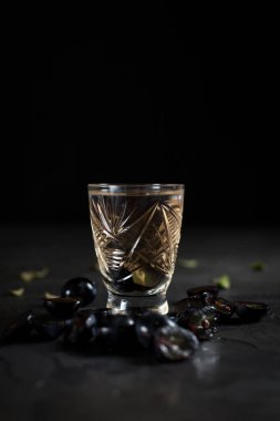 şeffaf bir içki ve karanlık bir arka plan üzerinde üzüm kesimleri ile cam