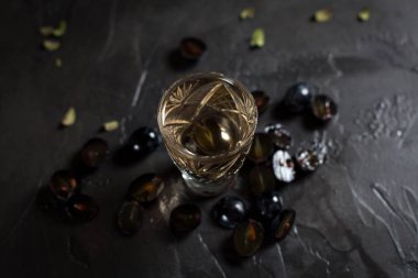 şeffaf bir içki ve karanlık bir arka plan üzerinde üzüm kesimleri ile cam