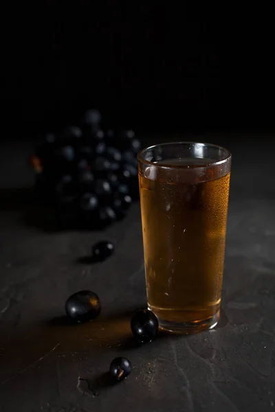 Бокал свежего виноградного сока и кучка сочного темного винограда на темном фоне — стоковое фото