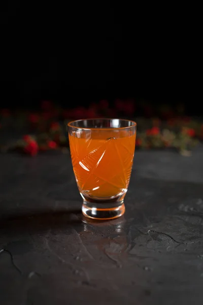 Een glas vers oranje drankje en rode bessen op een donkere achtergrond — Stockfoto