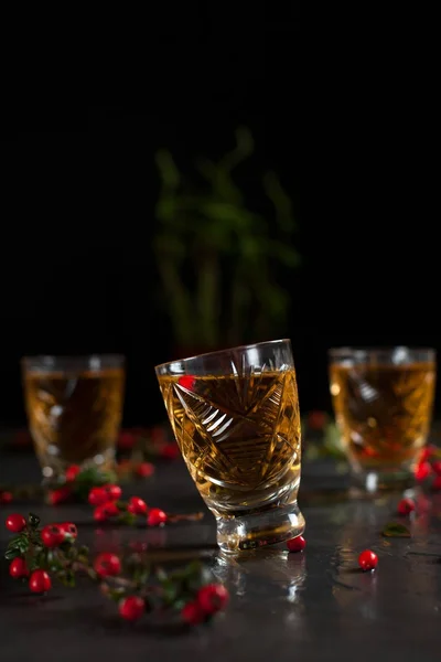 glasses with orange drink and branches with red berries on a dark wet background