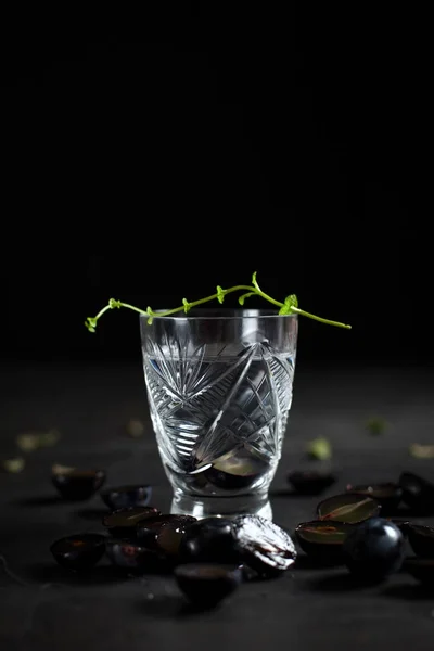 Vidro com uma bebida transparente e segmentos de uva em um fundo escuro — Fotografia de Stock