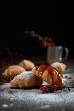 kırıntıları, pudra şekeri, karamel, çilek ve karanlık bir arka plan üzerinde kırmızı meyveler ile bir bardak ile birkaç tüm ay çöreği