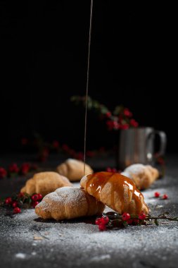 kırıntıları, pudra şekeri, karamel, çilek ve karanlık bir arka plan üzerinde kırmızı meyveler ile bir bardak ile birkaç tüm ay çöreği
