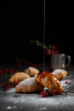 kırıntıları, pudra şekeri, karamel, çilek ve karanlık bir arka plan üzerinde kırmızı meyveler ile bir bardak ile birkaç tüm ay çöreği