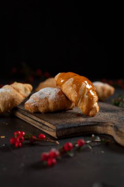 birkaç bütün kruvasan kırıntıları, pudra şekeri, karamel, ahşap kesme tahtası ve karanlık bir arka plan üzerinde kırmızı meyveler