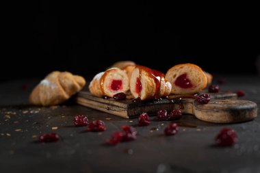 kruvasan doldurma, kırmızı dut ile kesme ile pudra şekeri serpilir ve Tepesi ve reçel, ahşap tahta bir karanlık kesme ve kırmızı meyveler ile karanlık bir arka plan üzerine dökülür