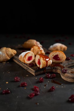 kruvasan doldurma, kırmızı dut ile kesme ile pudra şekeri serpilir ve Tepesi ve reçel, ahşap tahta bir karanlık kesme ve kırmızı meyveler ile karanlık bir arka plan üzerine dökülür