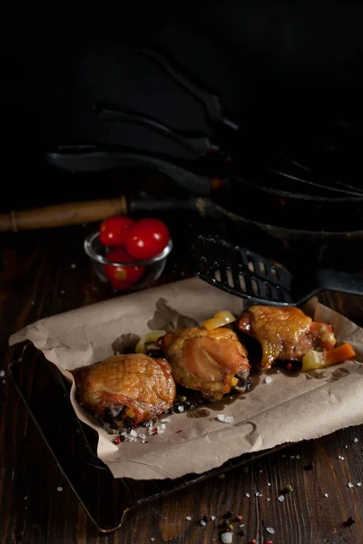 Baked juicy chicken with a crispy crust, in spices, on a black plate, on baking paper, large sea salt on a dark wooden background — Stock Photo, Image