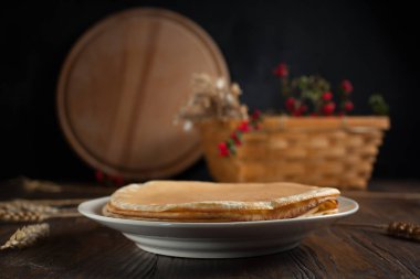 bir yığın krep, spikelets, yuvarlak kesme tahtası, dalları kırmızı meyveler ve koyu ahşap bir masa üzerinde meyveleri ile sepet