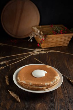 bir yığın krep, çilek, tanımlama bilgileri, ekşi krema ve parşömen üzerine koyu ahşap bir masa üzerinde bir kesme tahtası