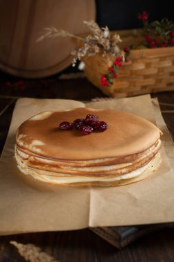 bir yığın krep, spikelets, yuvarlak kesme tahtası, dalları kırmızı meyveler ve koyu ahşap bir masa üzerinde meyveleri ile sepet
