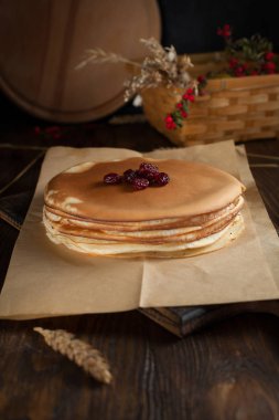 bir yığın krep, spikelets, yuvarlak kesme tahtası, dalları kırmızı meyveler ve koyu ahşap bir masa üzerinde meyveleri ile sepet