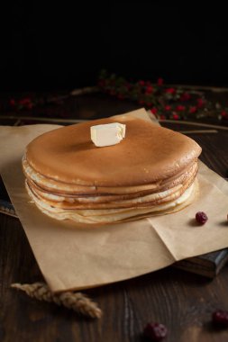 bir yığın krep, çilek, tanımlama bilgileri, tereyağı ve parşömen üzerine koyu ahşap bir masa üzerinde bir kesme tahtası