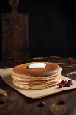 bir yığın krep, çilek, tanımlama bilgileri, ekşi krema ve parşömen üzerine koyu ahşap bir masa üzerinde bir kesme tahtası