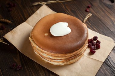 bir yığın krep, çilek, tanımlama bilgileri, ekşi krema ve parşömen üzerine koyu ahşap bir masa üzerinde bir kesme tahtası