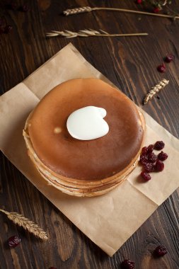 bir yığın krep, çilek, tanımlama bilgileri, ekşi krema ve parşömen üzerine koyu ahşap bir masa üzerinde bir kesme tahtası