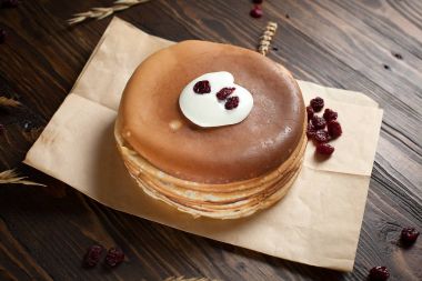 bir yığın krep, çilek, tanımlama bilgileri, ekşi krema ve parşömen üzerine koyu ahşap bir masa üzerinde bir kesme tahtası