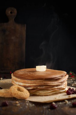 bir yığın krep, çilek, tanımlama bilgileri, tereyağı ve parşömen üzerine koyu ahşap bir masa üzerinde bir kesme tahtası