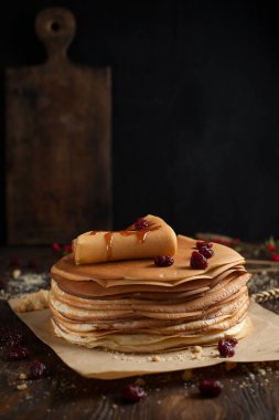 yığın krep katlanmış, gözleme, çilek, kurabiye, pudra şekeri ve koyu ahşap bir masa üzerine parşömen üzerine karamel şurup serpilir