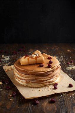 yığın krep katlanmış, gözleme, çilek, kurabiye, pudra şekeri ve koyu ahşap bir masa üzerine parşömen üzerine karamel şurup serpilir